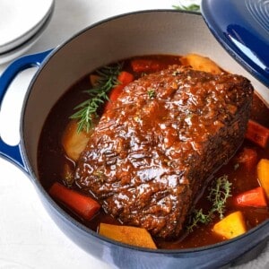 a fully cooked beef pot roast, onions, carrots, potatoes, and gravy in a blue dutch oven