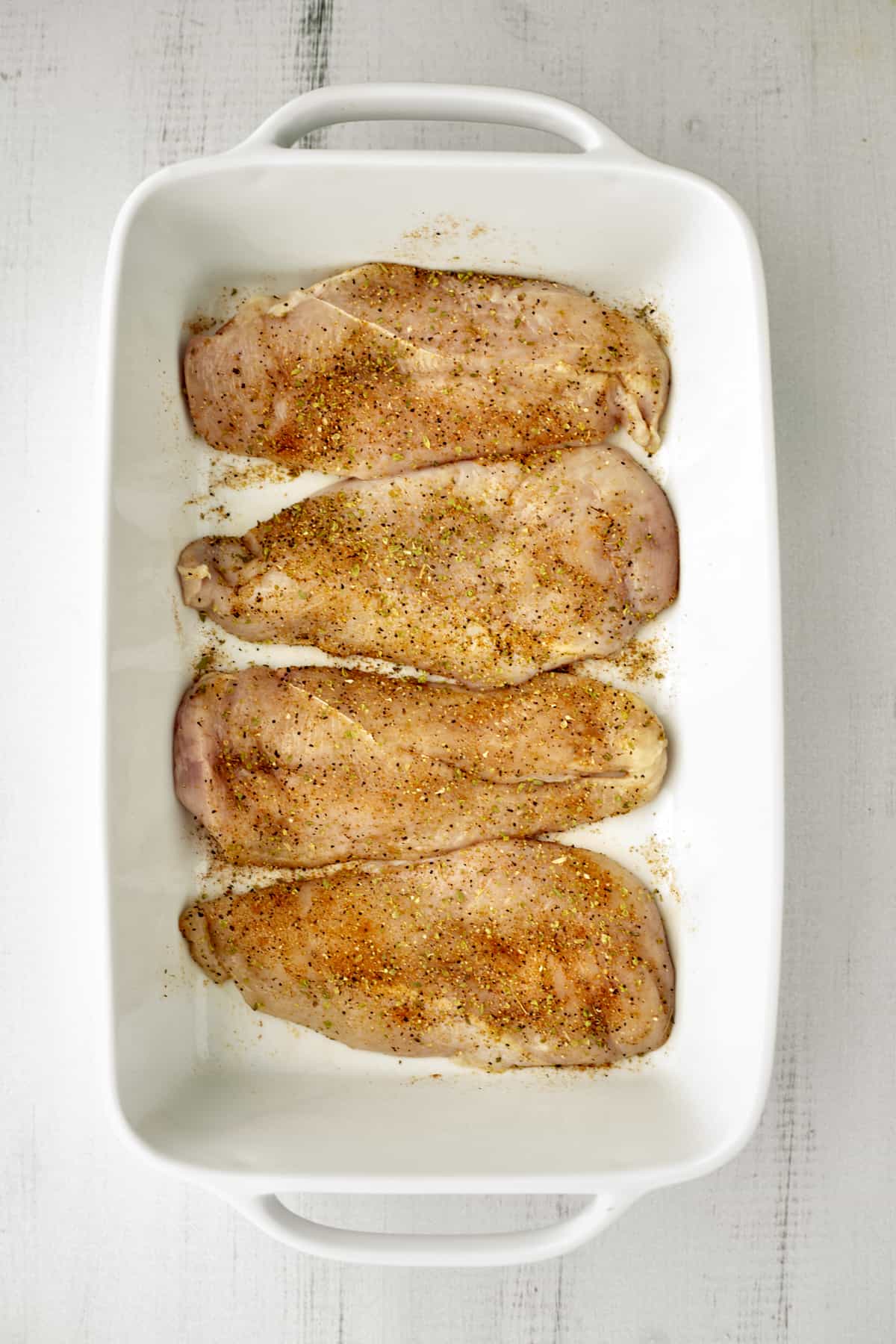 four seasoned chicken breasts in a white baking dish