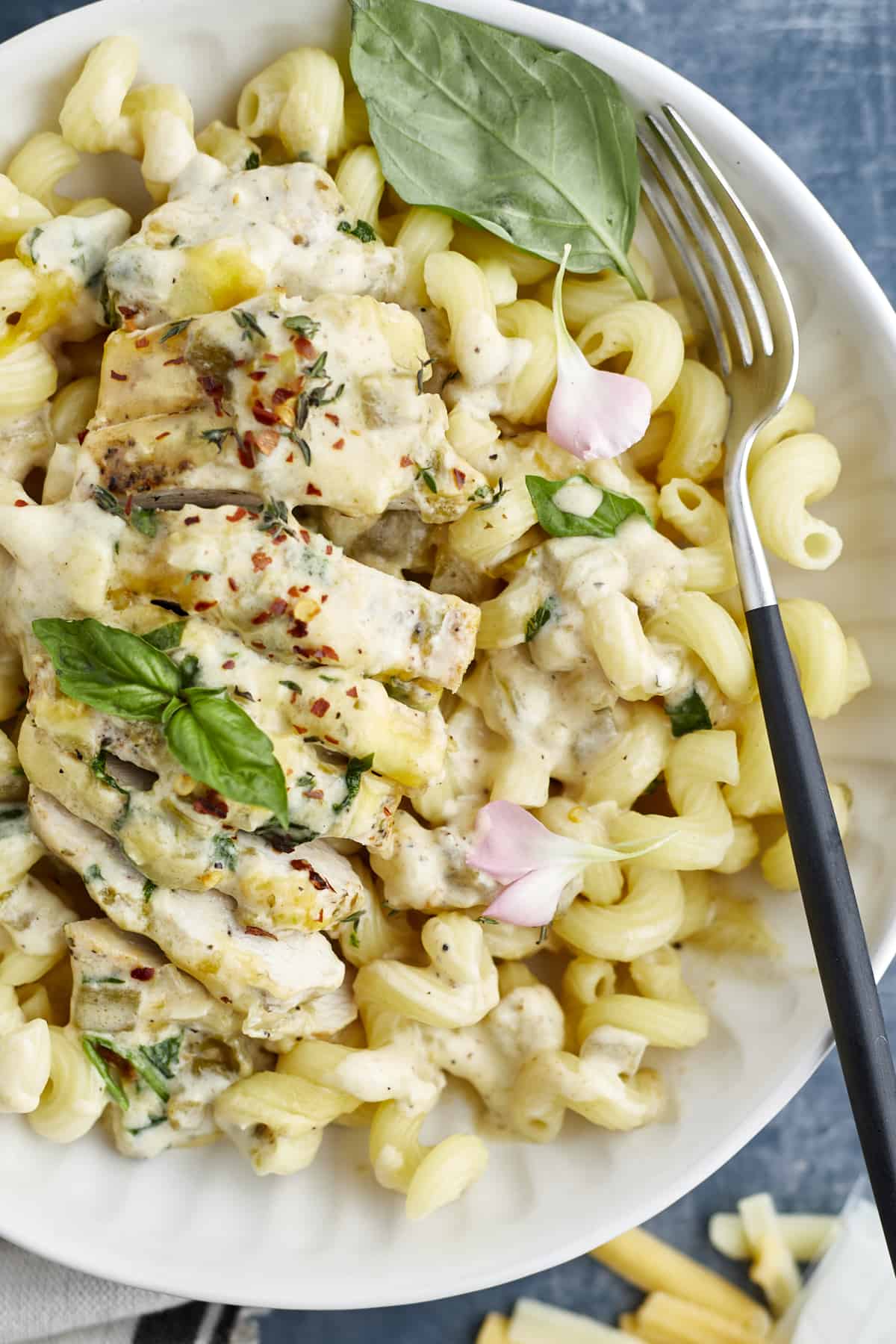 overhead image of cheesy chicken in a white bowl on top of cavatappi noodles with a fork on the side