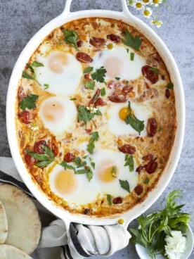 overhead image of 6 oven baked eggs in a baking dish with feta and veggies.