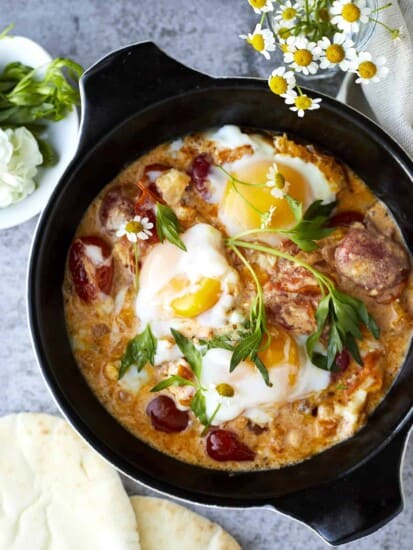 overhead image of a skillet full of oven baked eggs, feta, and vegetables.