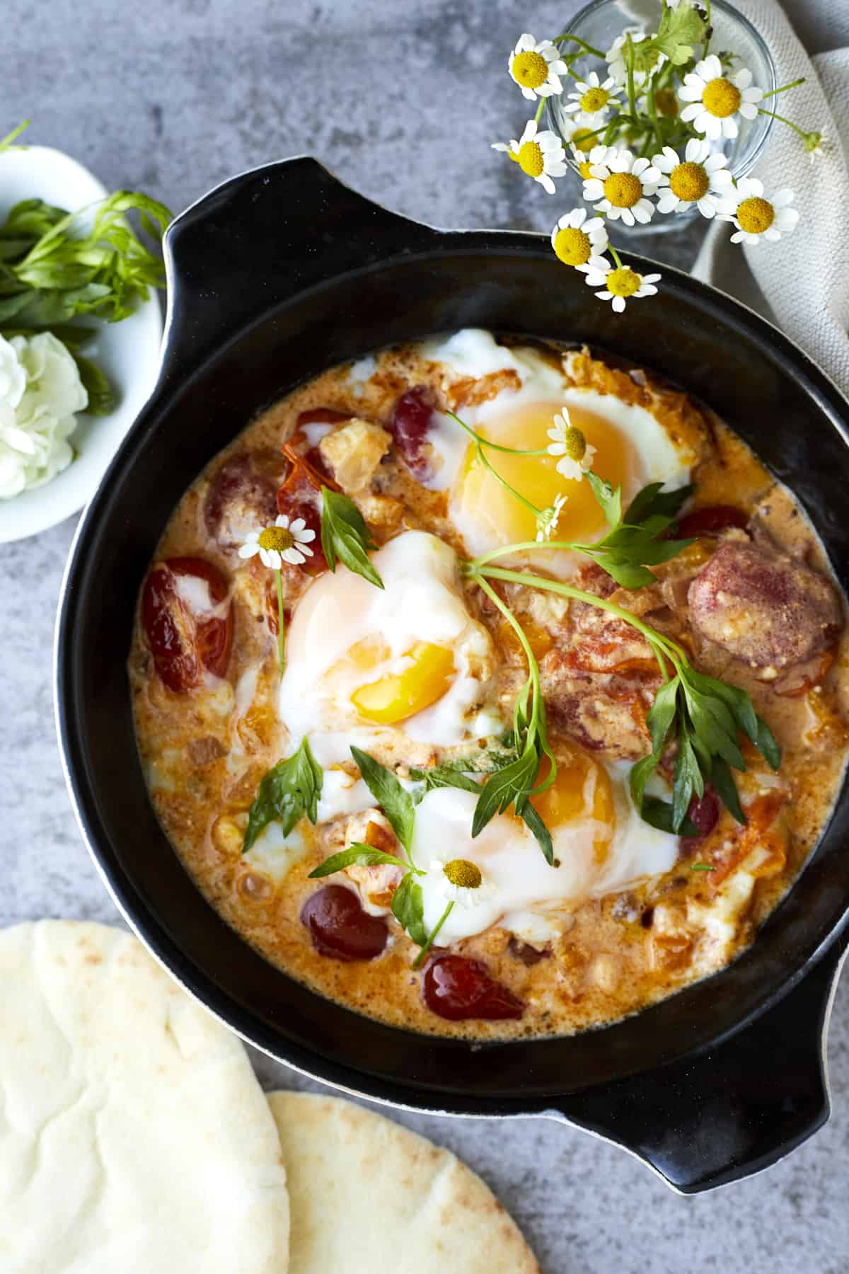 overhead image of oven baked eggs in a cast iron skillet with feta and veggies topped with fresh herbs.