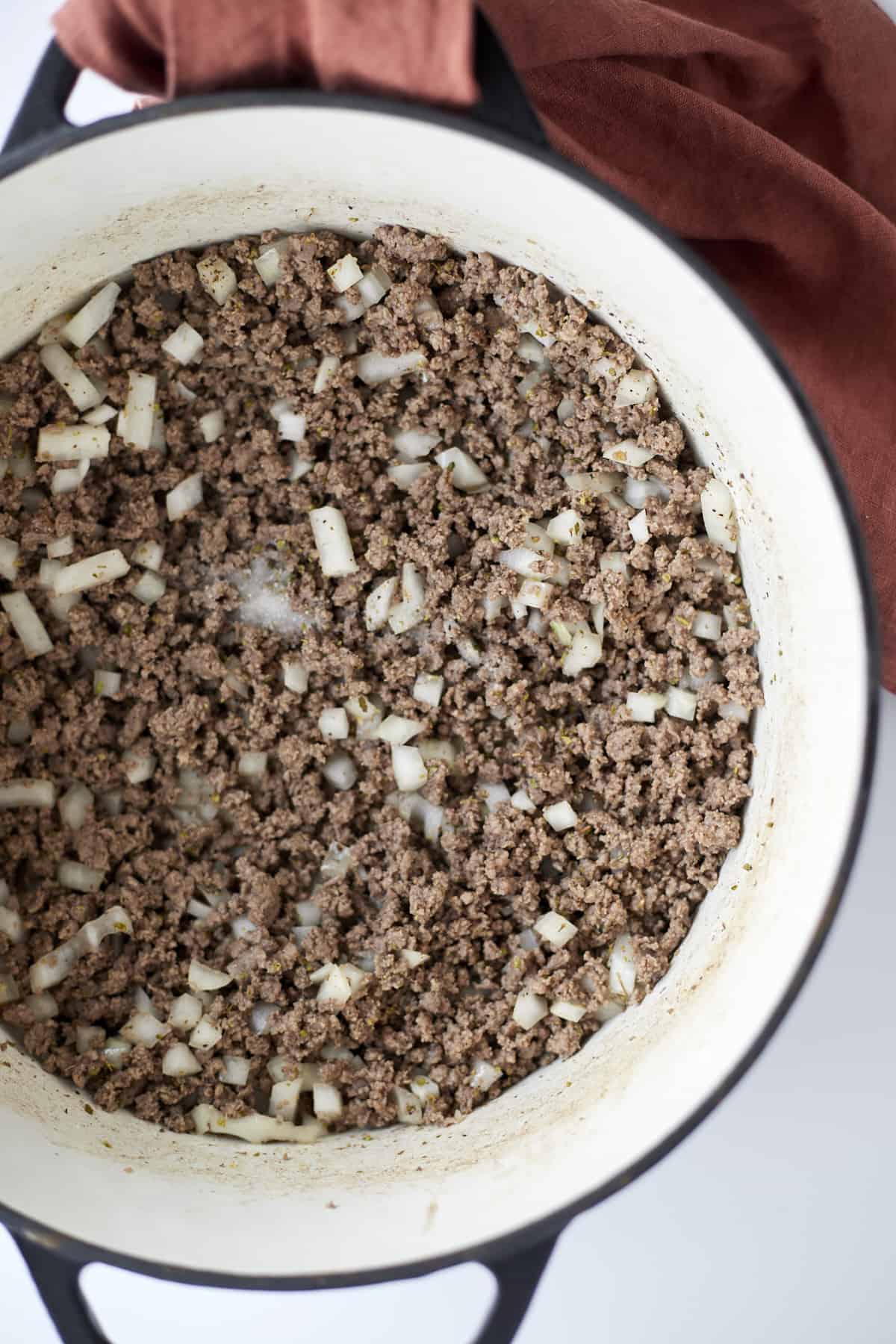 overhead image of a large pot with cooked ground beef, chopped onions, and garlic.