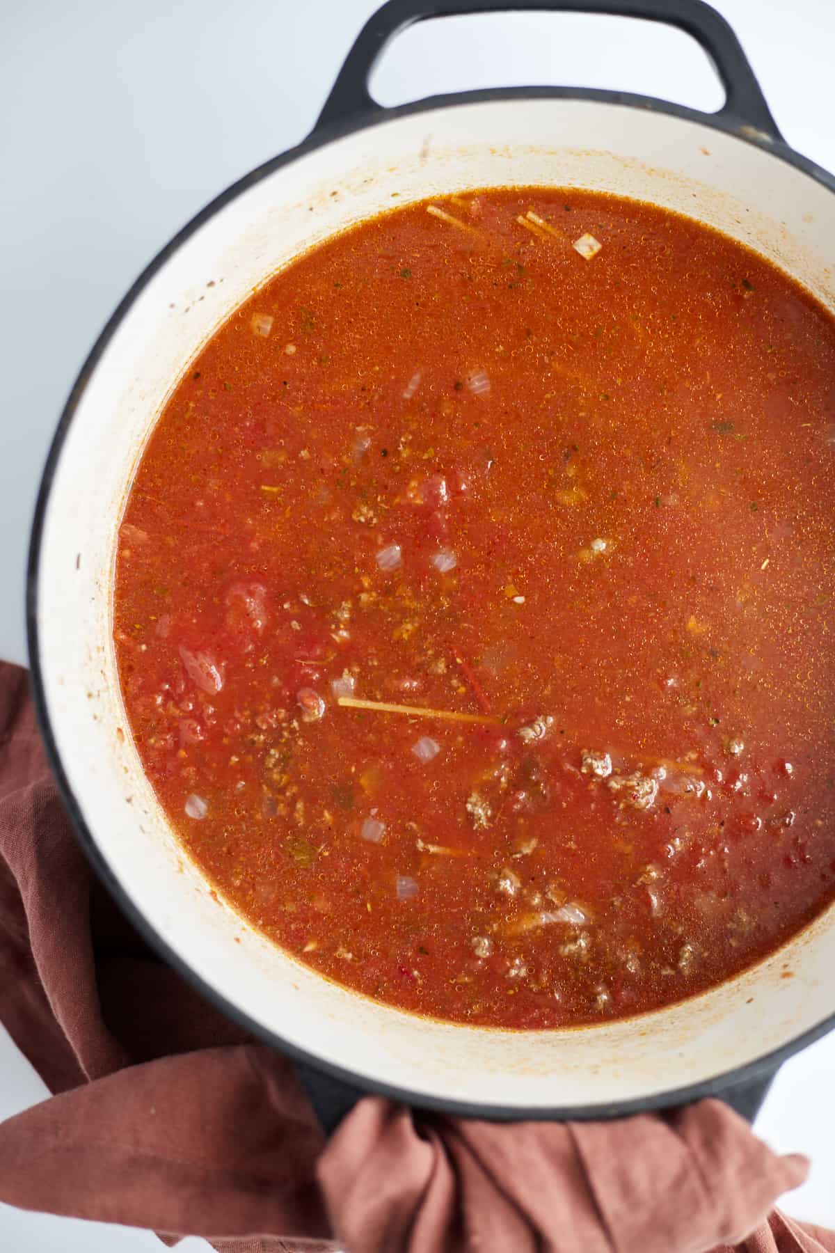 overhead image of a large pot full of beef, onions, and tomato sauce to make one pot spaghetti.