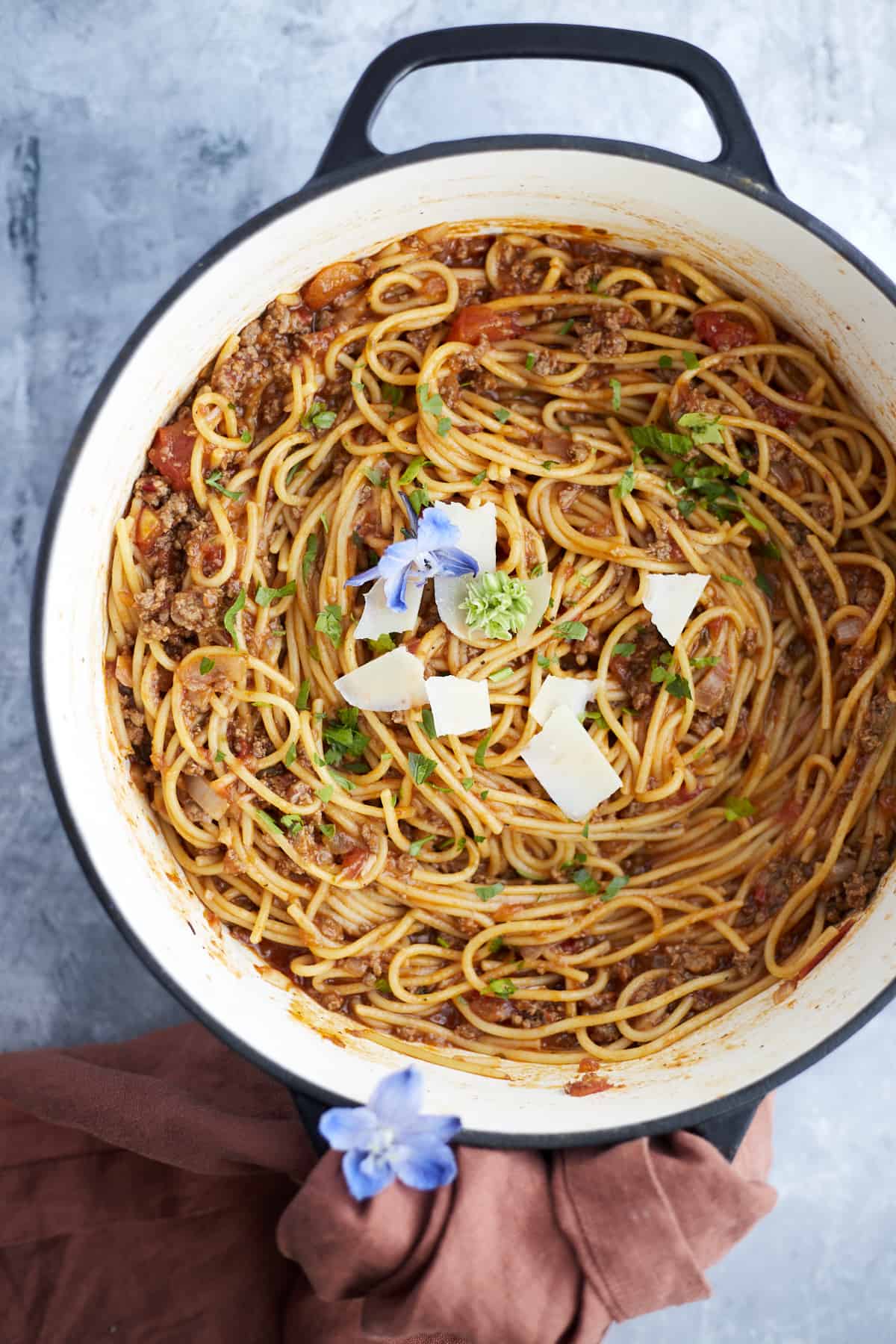 overhead image of one pot spaghetti with ground beef in a large pot topped with fresh herbs and shaved Parmesan cheese.