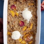 overhead image of a baked peach crisp topped with two scoops of vanilla ice cream with a serving missing out of the bottom righthand corner.