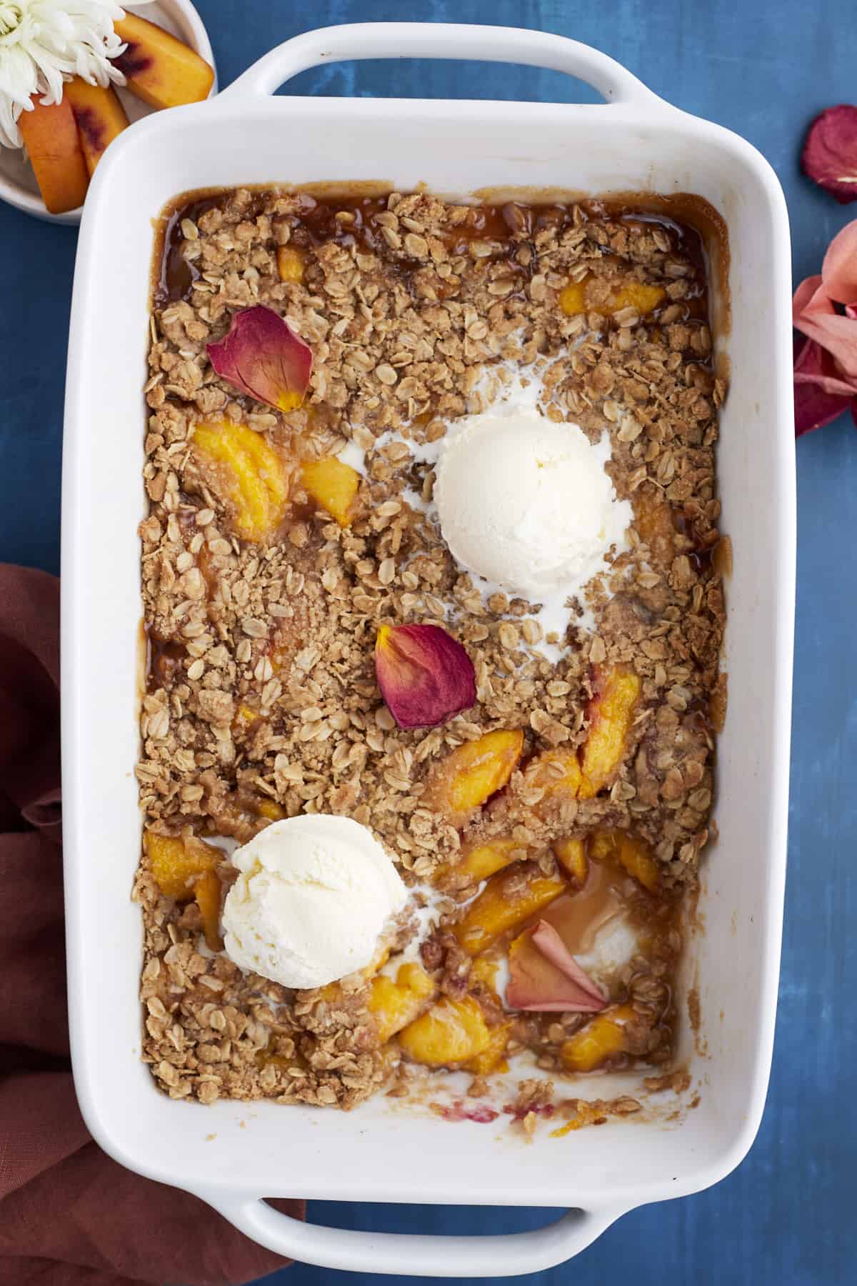 overhead image of a baked peach crisp topped with two scoops of vanilla ice cream and a serving missing from the bottom right corner.