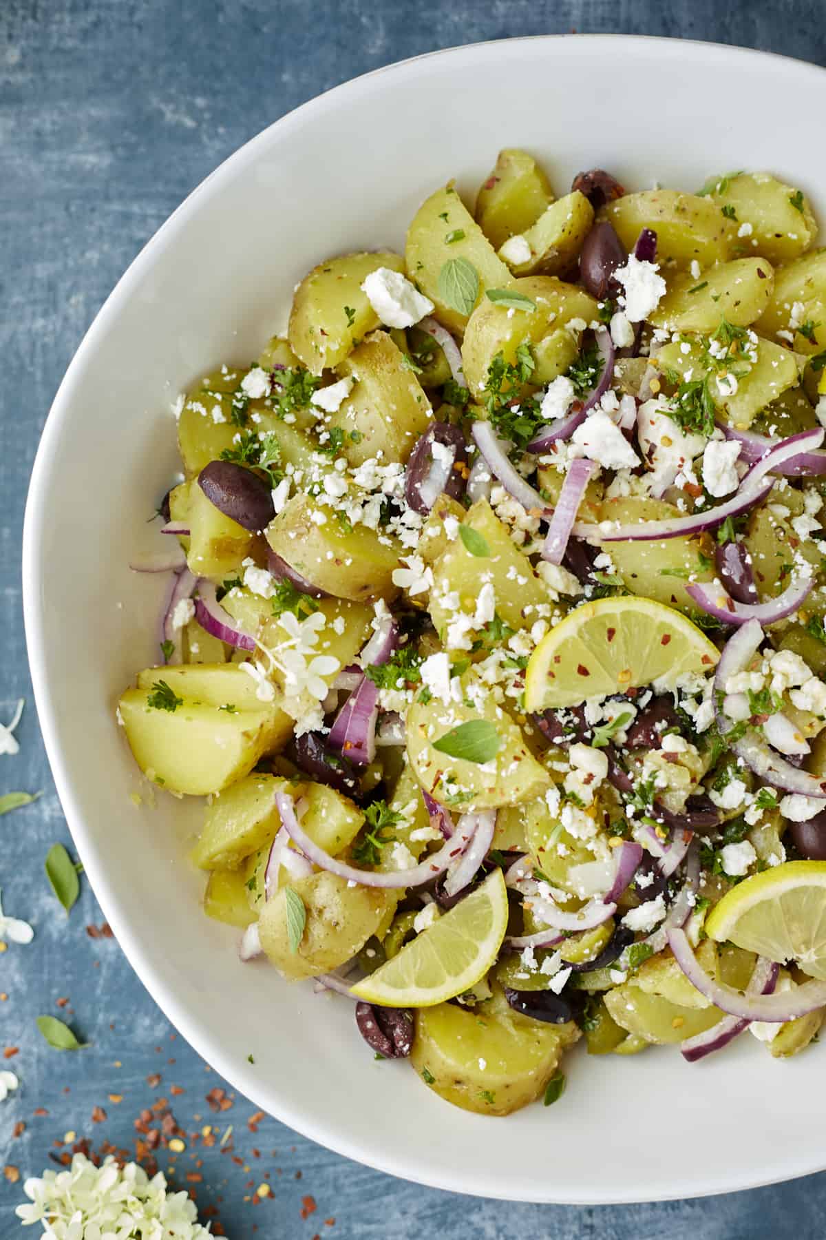 a bowl of lemon greek potatoes with red onions, olives, feta, fresh herbs, and lemon wedges