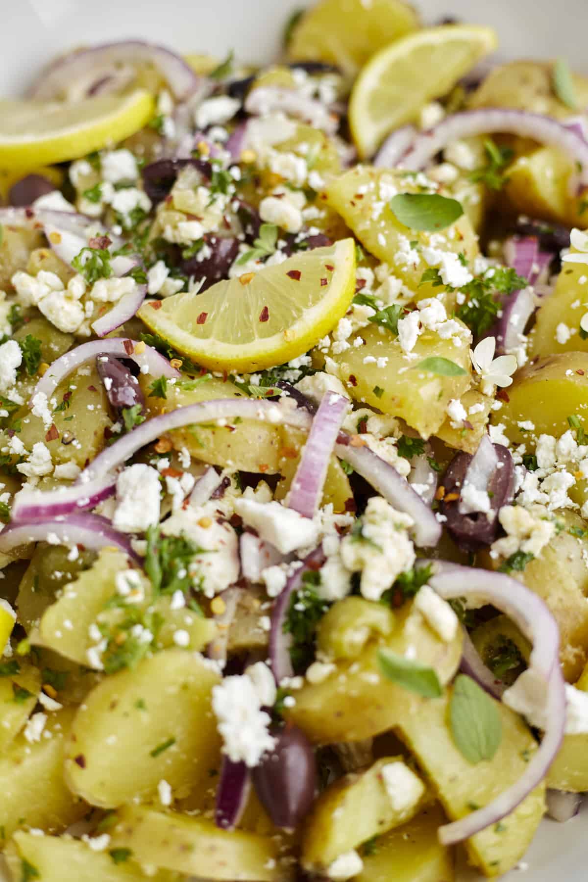 close up image of lemon greek roasted potatoes topped with feta, red onion, and lemon wedges