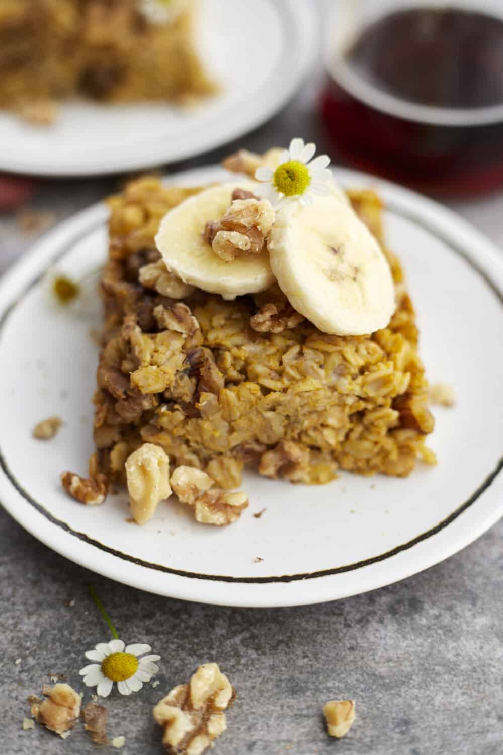 a white plate with a piece of baked pumpkin oatmeal topped with nuts and banana coins