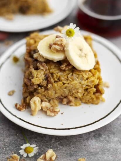 a white plate with a piece of baked pumpkin oatmeal topped with nuts and banana coins