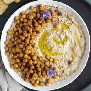 overhead image of a white bowl full of baba ganoush topped with crispy chickpeas with crackers on the side