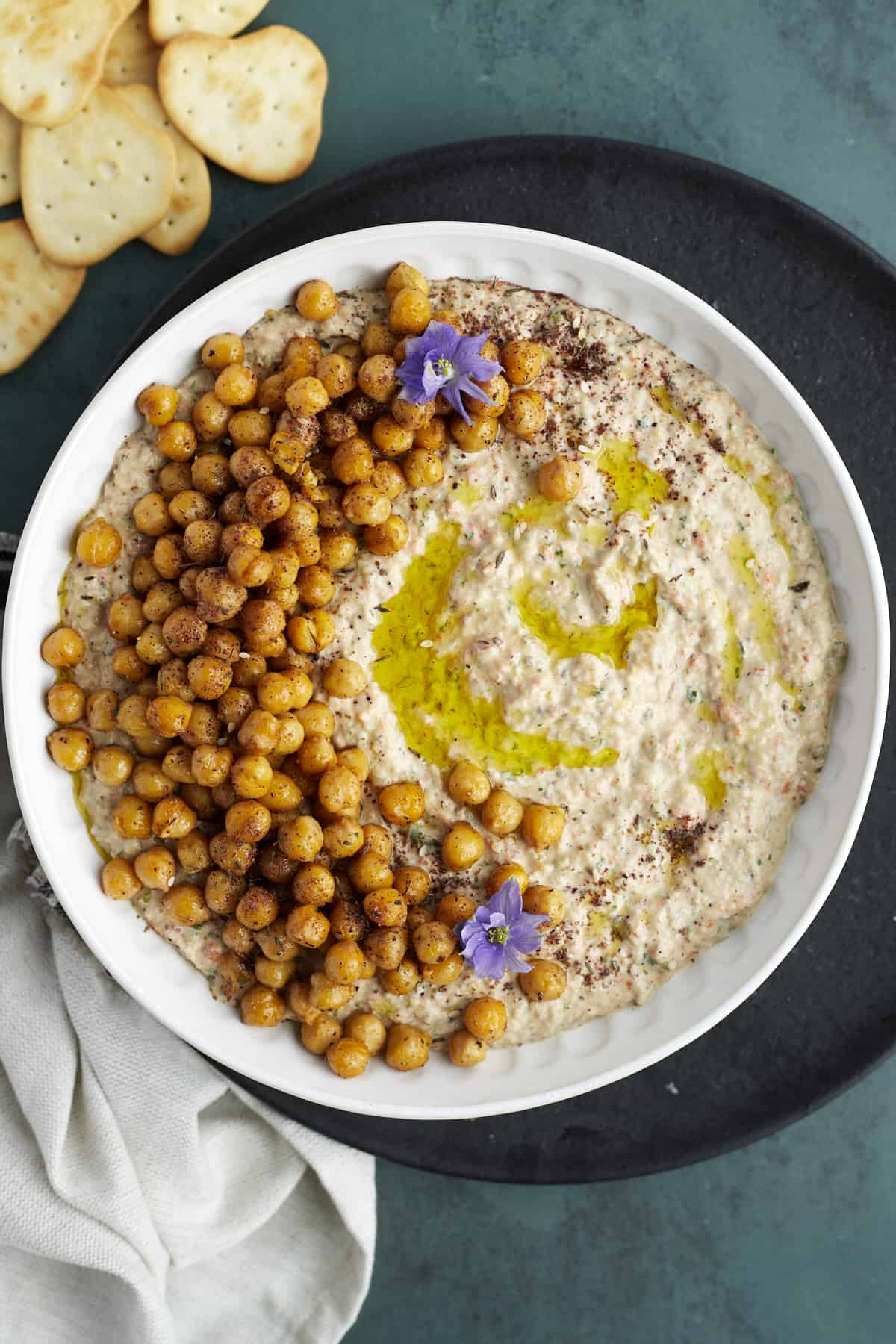 overhead image of a white bowl full of baba ganoush topped with crispy chickpeas with crackers on the side