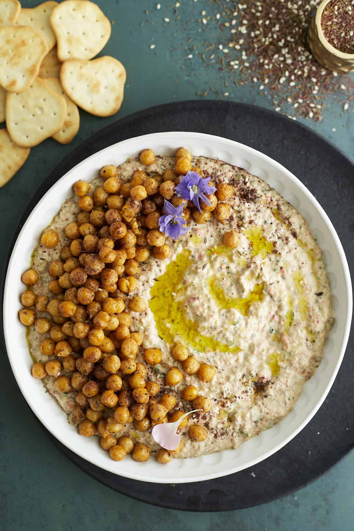 overhead image of a white bowl of baba ganoush topped with chickpeas with crackers on the side