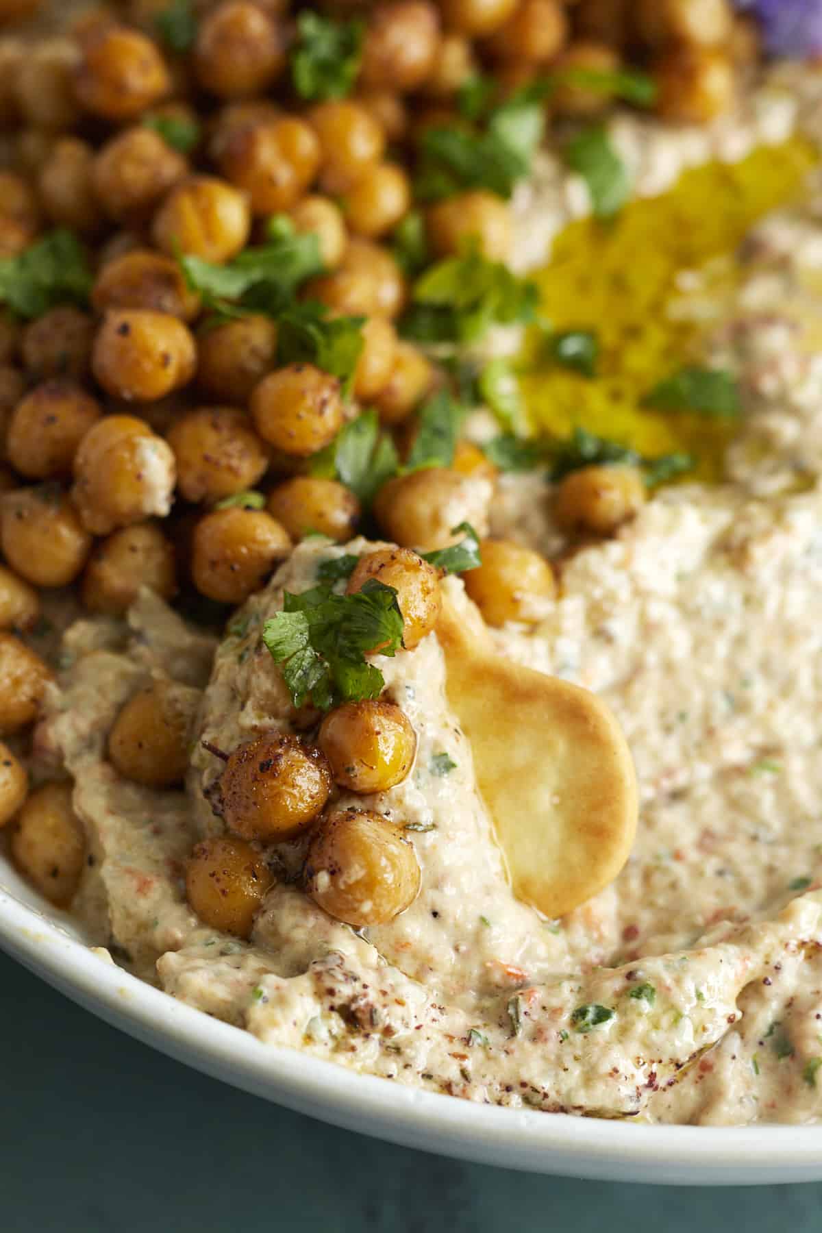 close up image of a cracker scooping up baba ganoush topped with crispy chickpeas