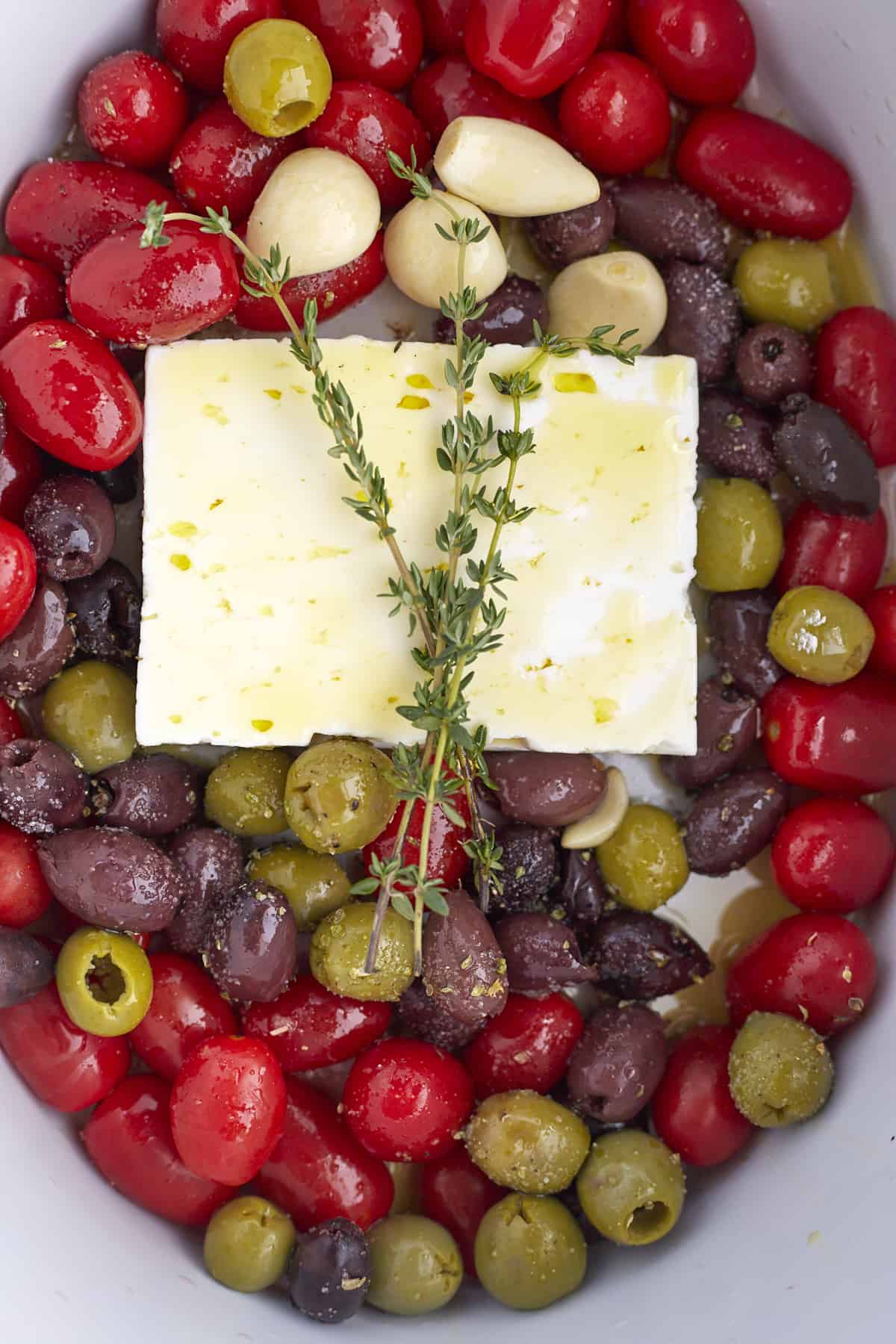 overhead image of tomatoes, olives, garlic, feta, and herbs in a slow cooker