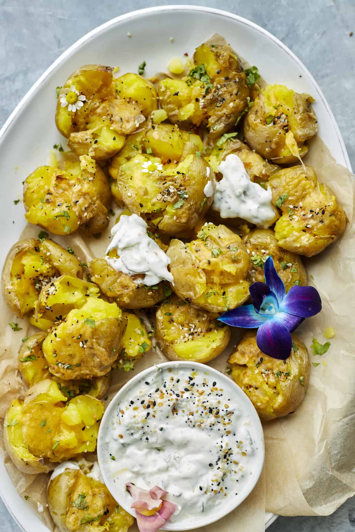 overehead image of smashed potatoes on a serving platter with a side of white creamy sauce