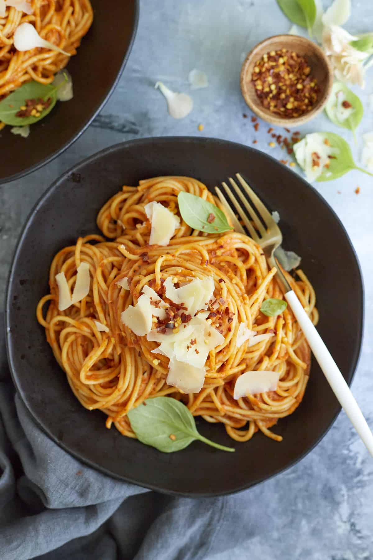 overhead image of a bowl of arrabiata sauce spaghetti topped with fresh Parmesan and basil with a fork on the side