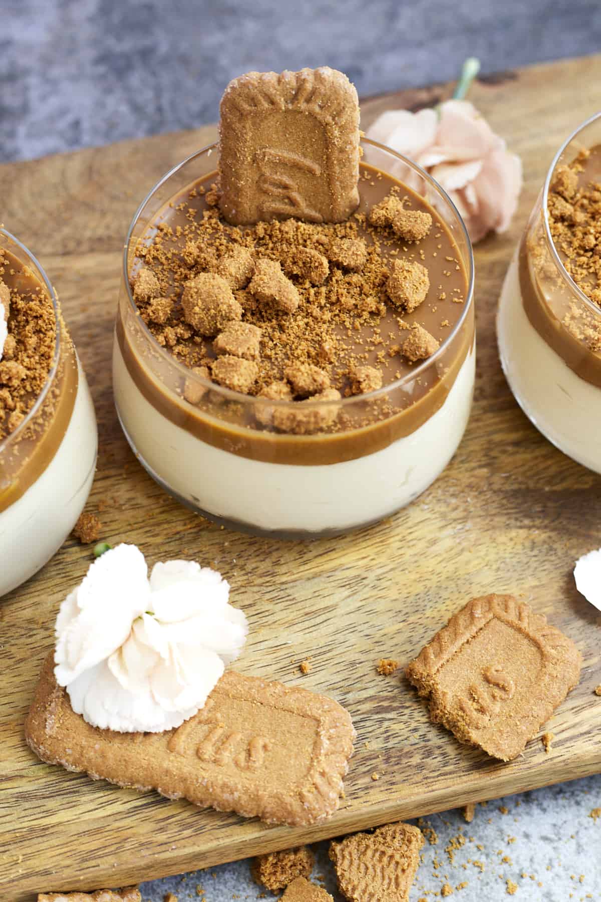 overehead image of jars of biscoff mousse topped with Biscoff spread and Biscoff cookies on a wooden board with Biscoff cookies scattered around