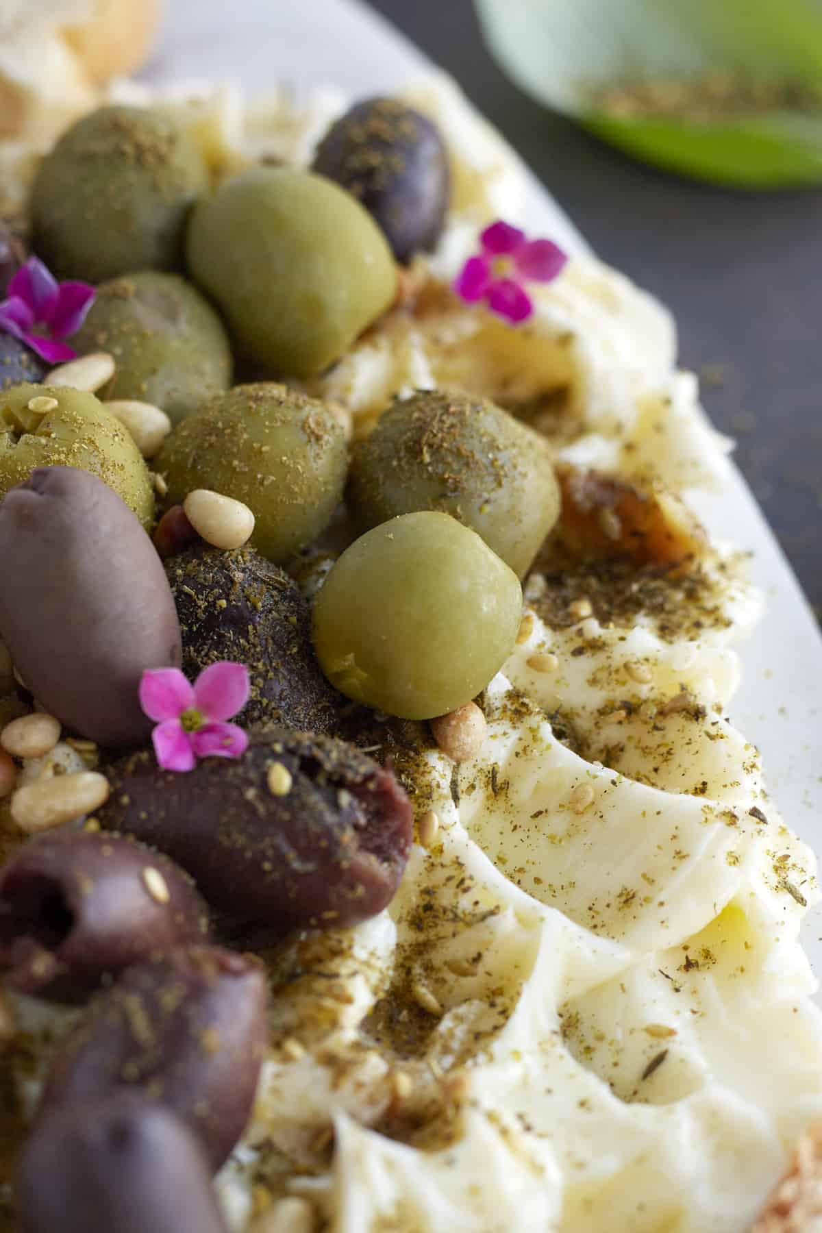 close up image of a butter board with olives, pine nuts, garlic, and seasonings