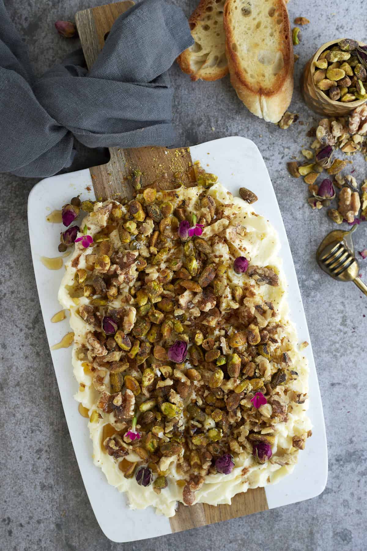 overhead image of a butter board topped with roasted walnuts, pistachios, honey, cinnamon, and salt