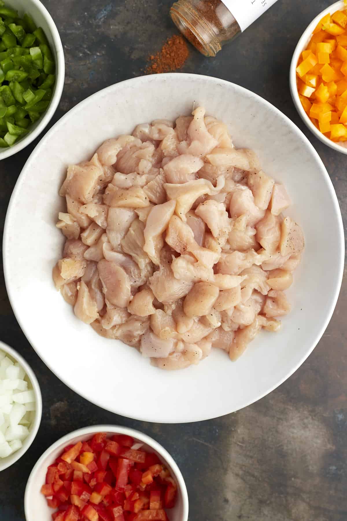 overhead image of bowls of raw chicken pieces, diced green, orange, and red peppers, diced onions, and seasoning