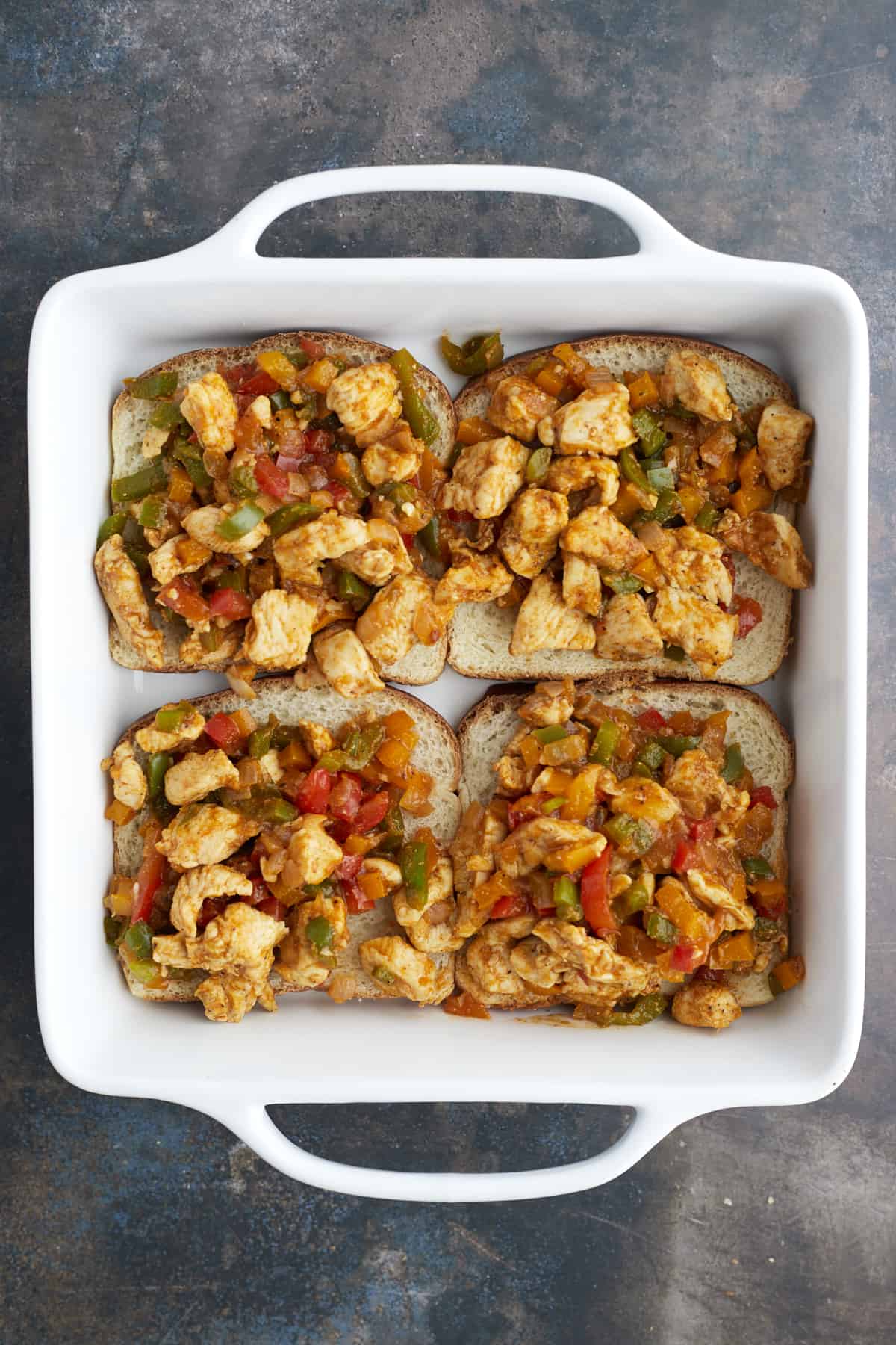 four pieces of bread in the bottom of a white baking dish topped with chicken fajita mixture