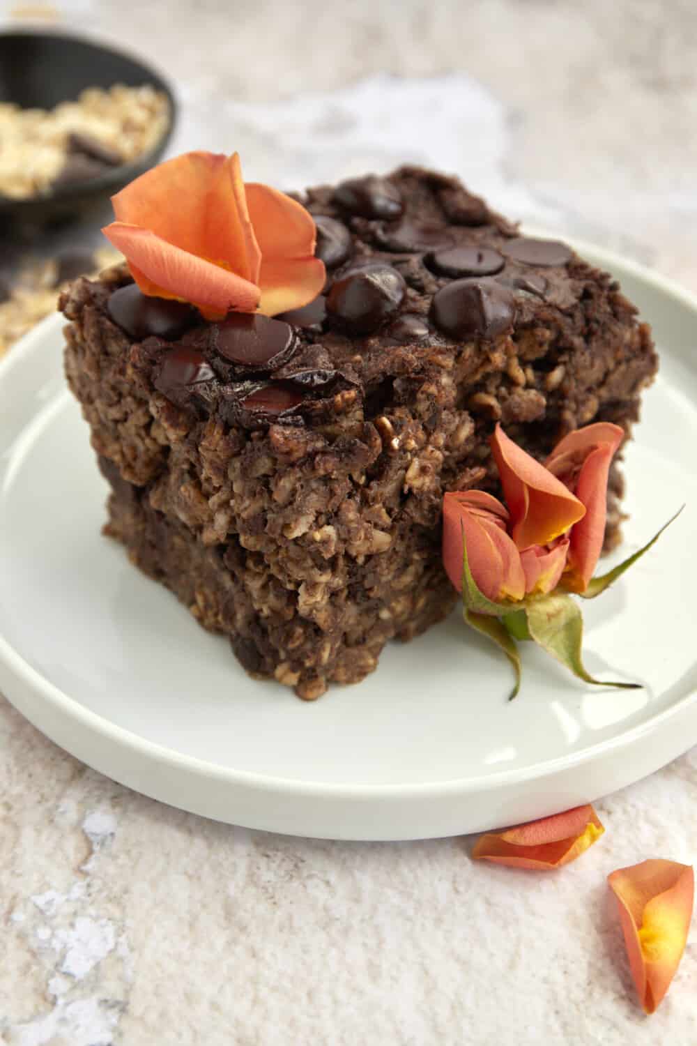 a sliced of chocolate baked oatmeal on a white plate topped with orange flower petals
