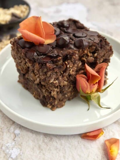 a sliced of chocolate baked oatmeal on a white plate topped with orange flower petals
