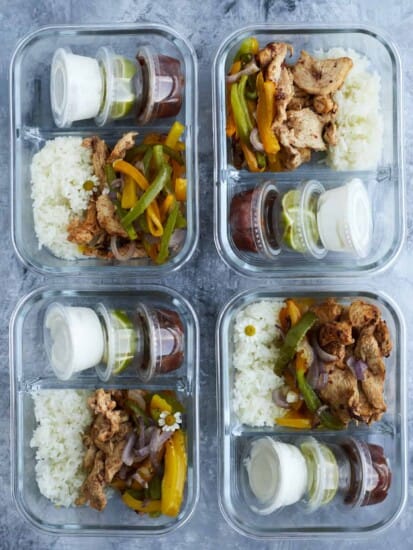 4 chipotle chicken meal prep boxes with onions, peppers, and sides of salsa, guacamole, and sour cream.