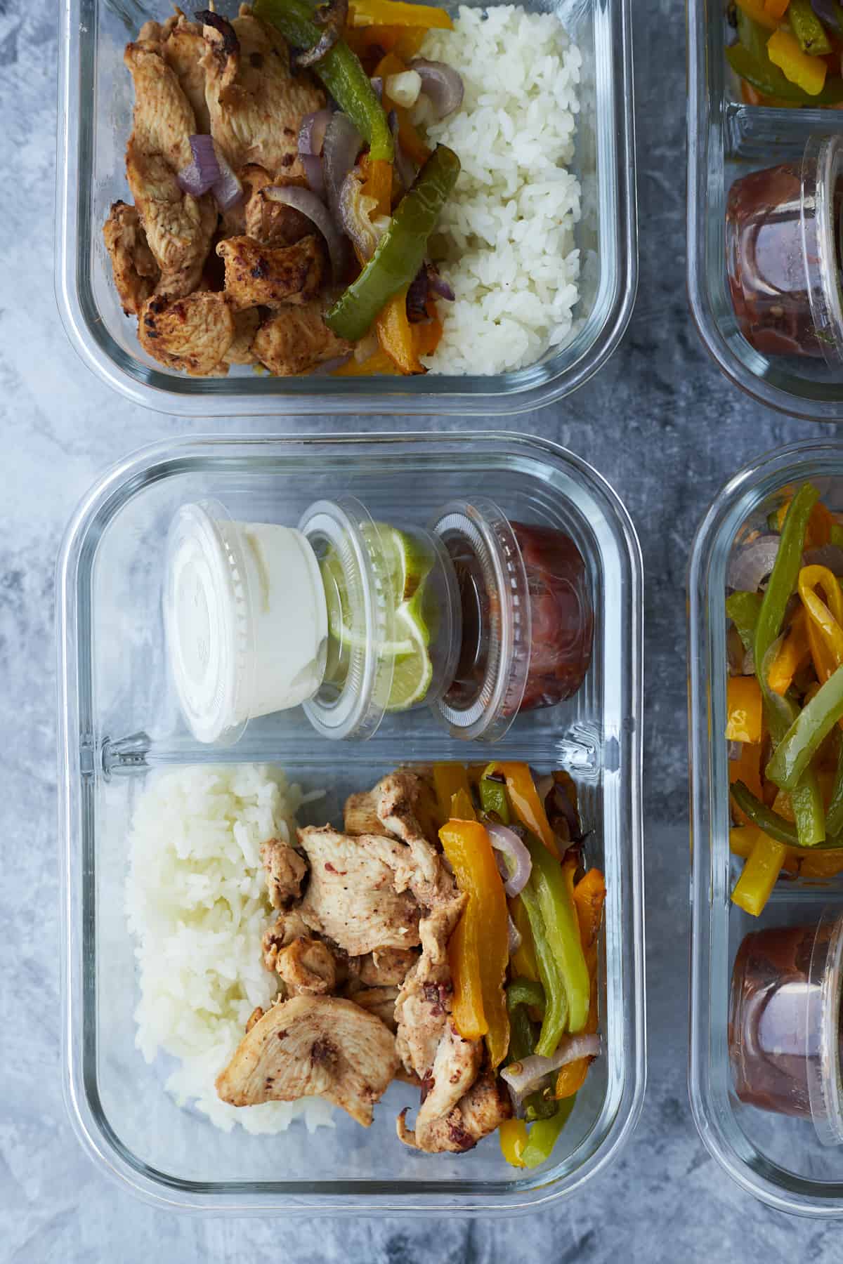 chipotle chicken in a meal prep box with onions, peppers, white rice, and small containers of salsa, guacamole, and sour cream on the side