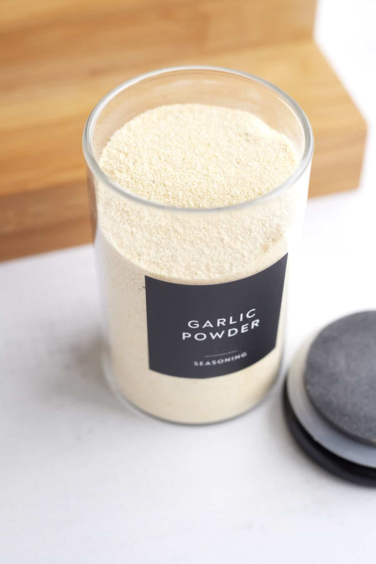 overhead image of a clear container with the black top next to it full of garlic powder with a black label reading garlic powder