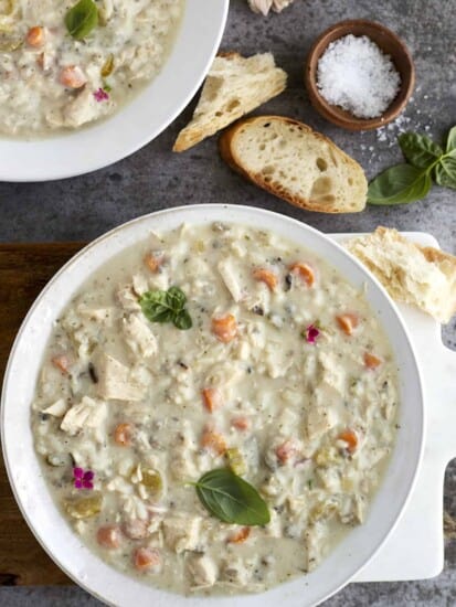 two bowls of crockpot chicken and wild rice soup with pieces of bread next to them