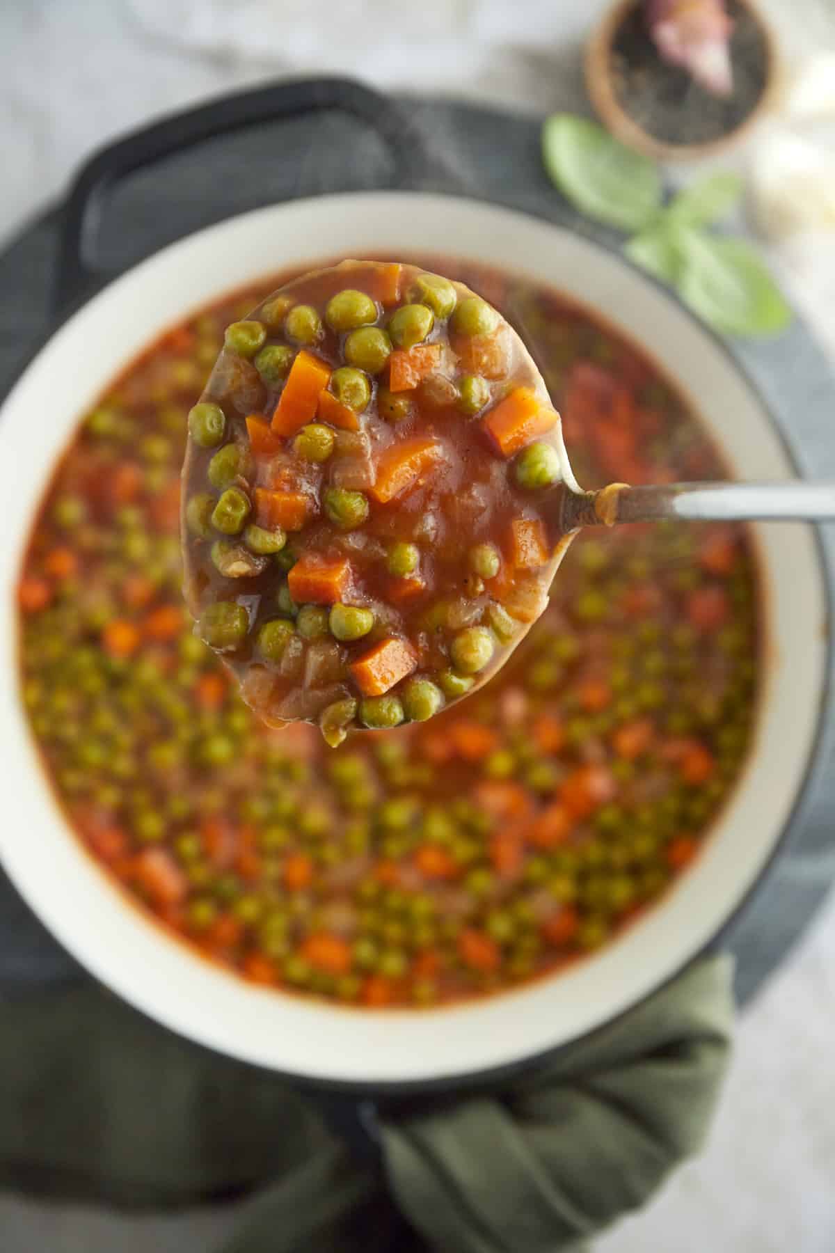 A ladle of pea and carrot vegetarian stew over a large pot