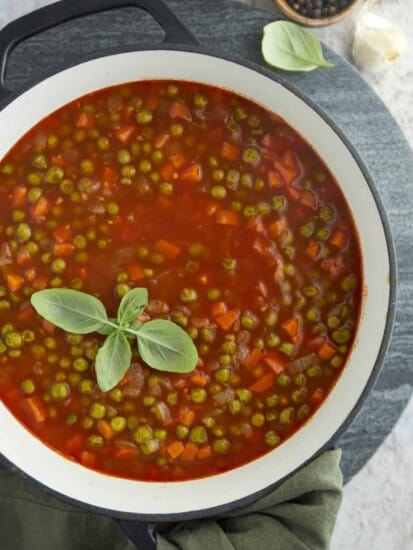 a large pot full of pea and carrot vegetarian stew topped with fresh herbs