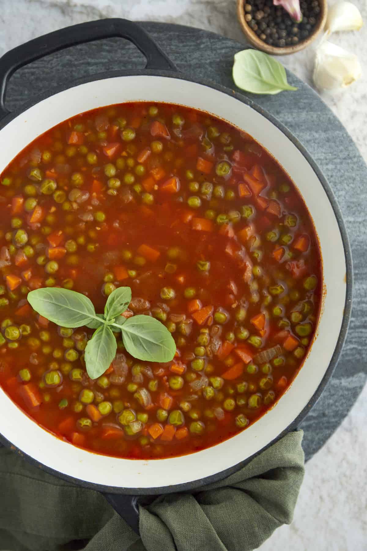 overhead image of pea and carrot vegetarian stew in a white bowl topped with fresh herbs