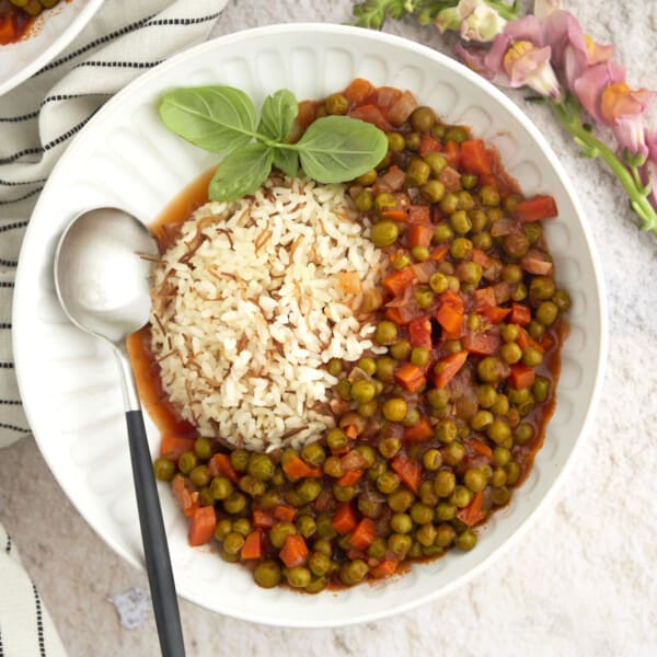 overhead image of pea and carrot stew with rice in a large white bowl topped with fresh herbs with a spoon on the side