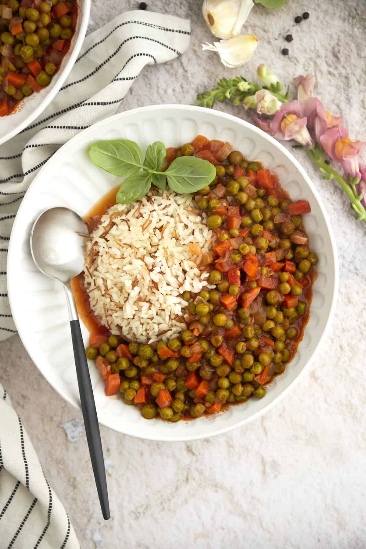 overhead image of pea and carrot stew with rice in a large white bowl topped with fresh herbs with a spoon on the side