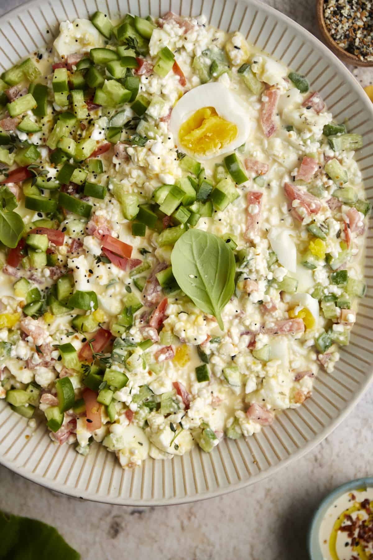 overhead image of the best egg salad recipe in a white bowl topped with herbs and sliced boiled eggs