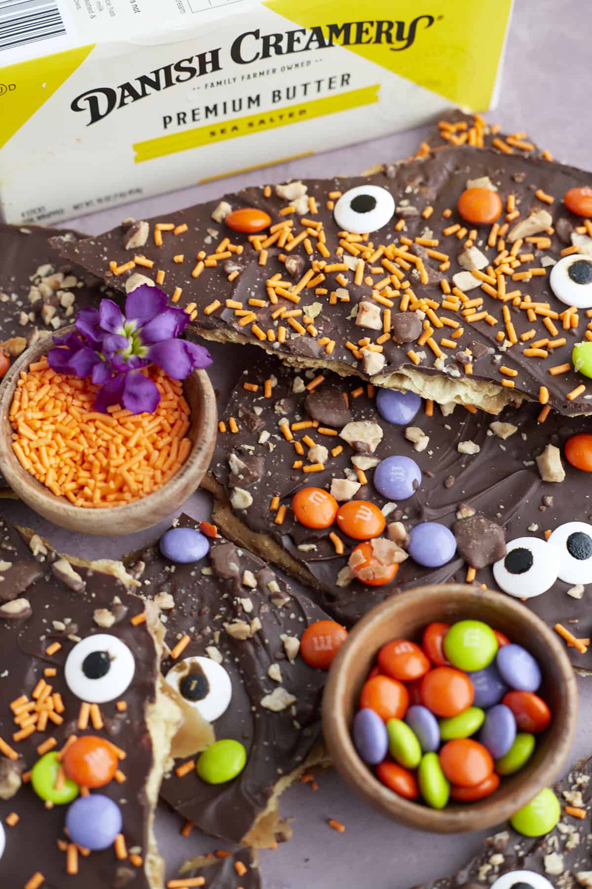 pieces of Halloween saltine crack candy with small bowls of m&ms and orange sprinkles in between 