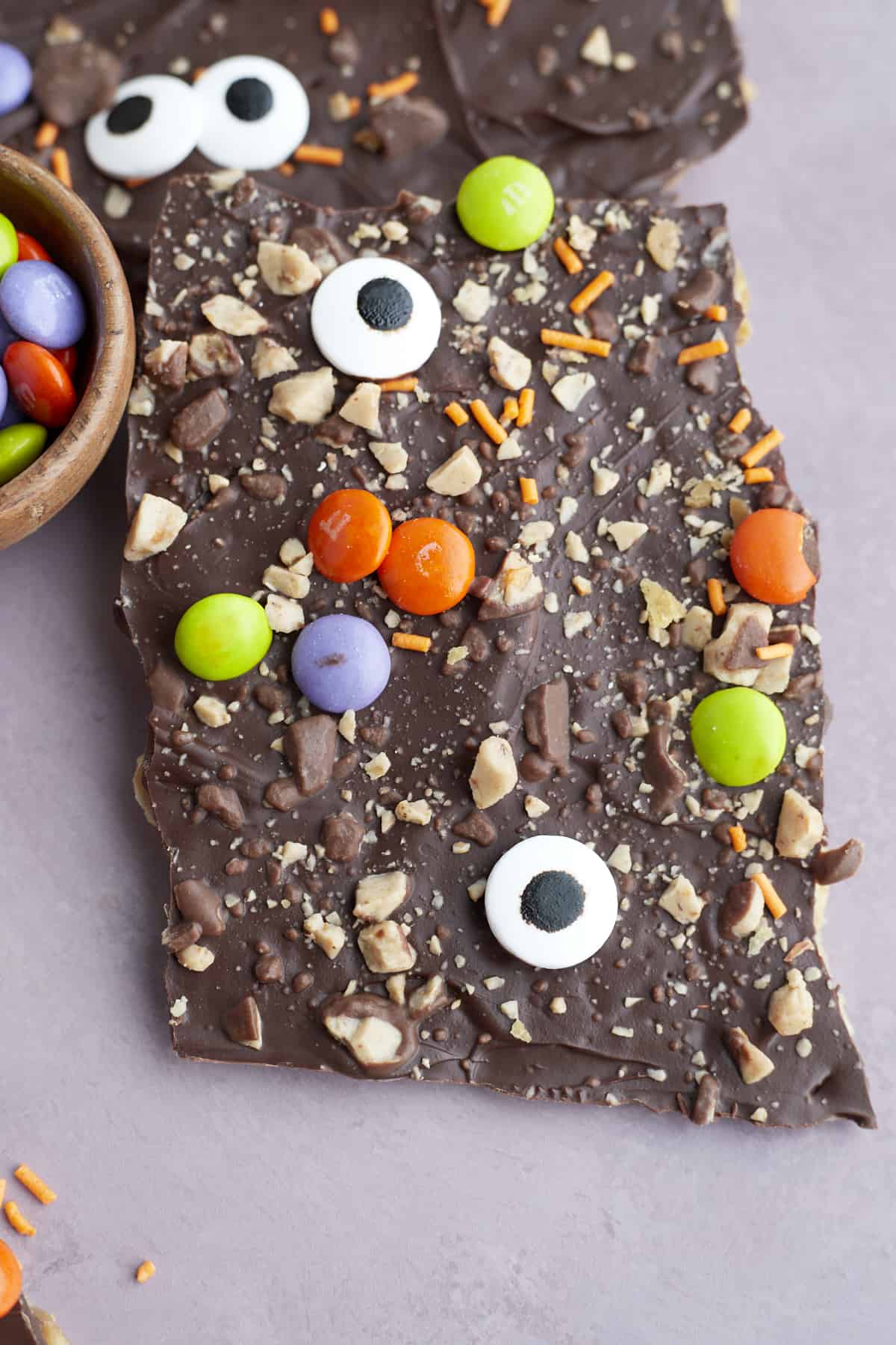 close up image of a piece of Halloween saltine crack candy topped with toffee bits, candy eyeballs, orange sprinkles, and M&Ms