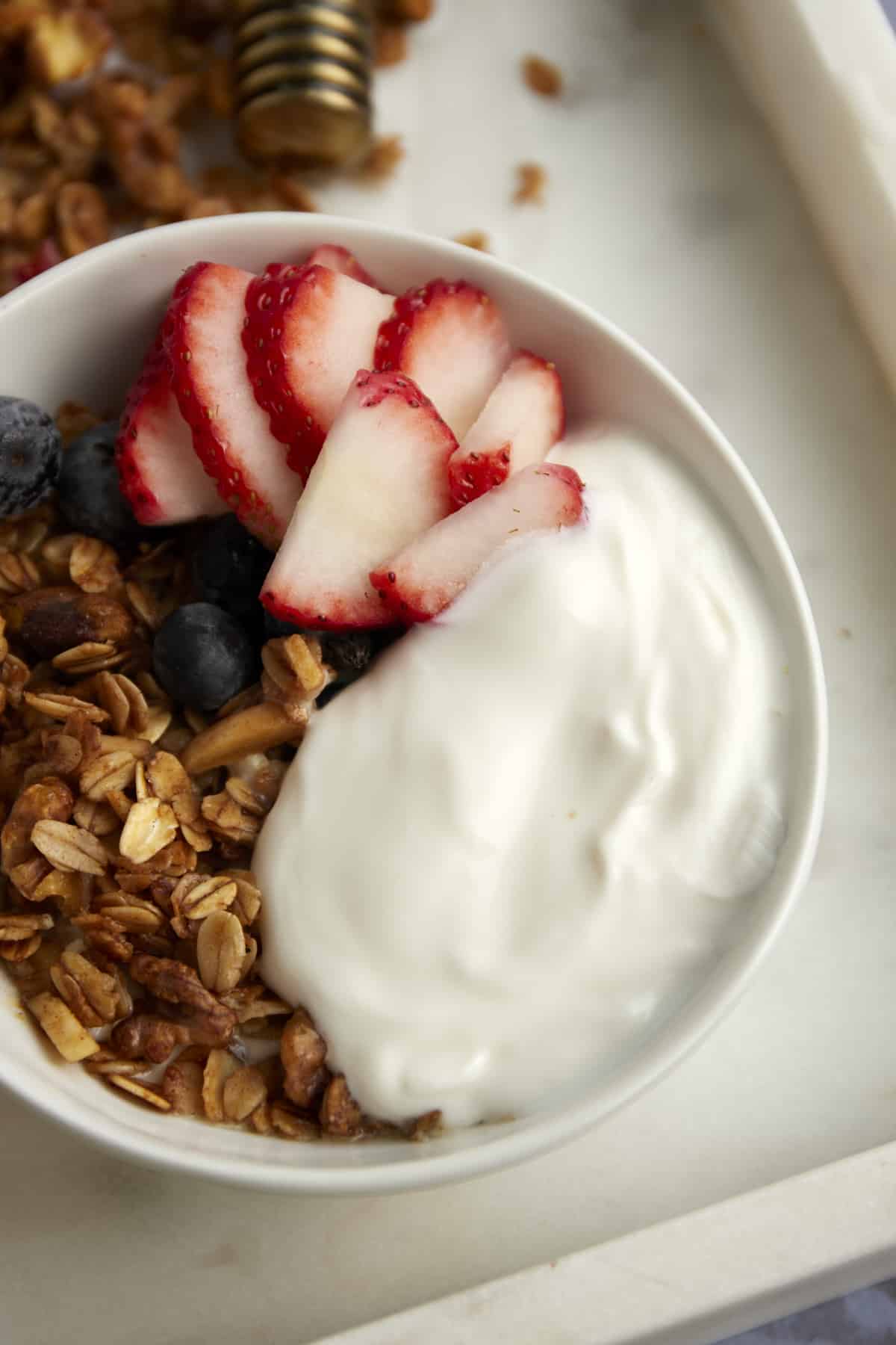 overhead image of a white bowl full of baklava granola, yogurt, strawberries, and blueberries