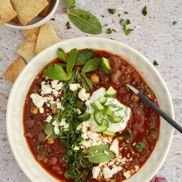 overhead image of a bowl of Middle Eastern Beef Chili topped with yogurt sauce, fresh herbs, feta, and cucumber