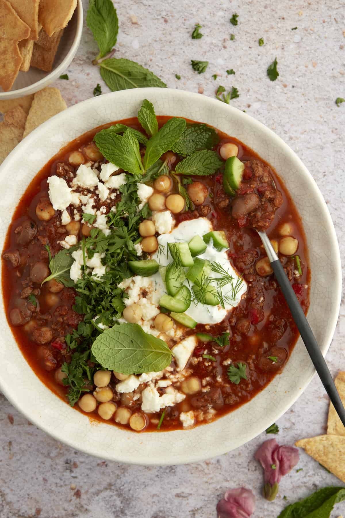 overhead image of a white bowl of Middle Eastern Beef Chili topped with feta, fresh herbs, and cucubers