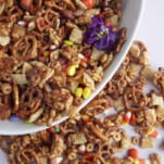 a white bowl full of Halloween snack mix with more snack mix overflowed onto the table next to it