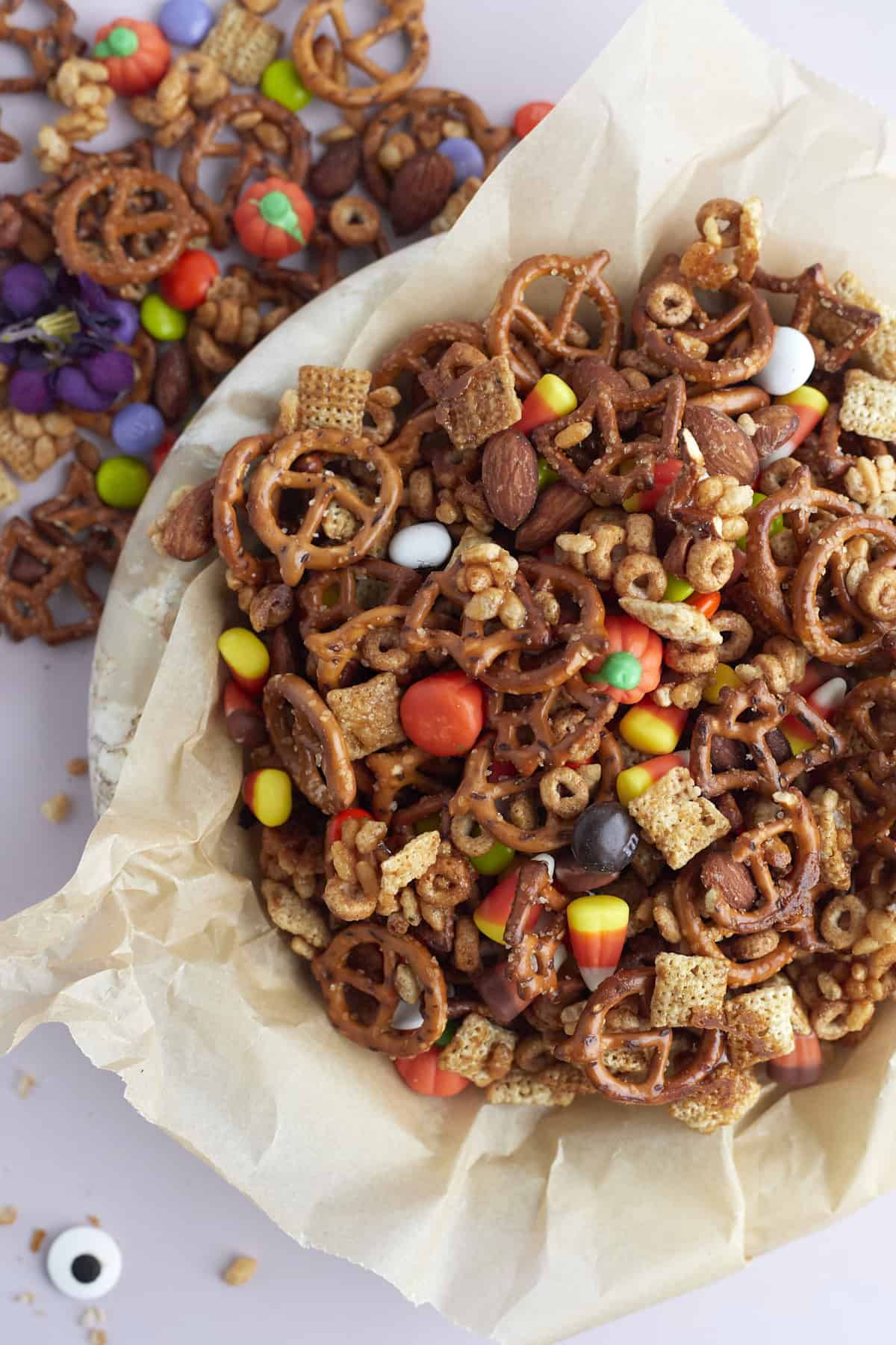 a parchment paper-lined bowl of Halloween snack mix with more snack mix on the table next to it