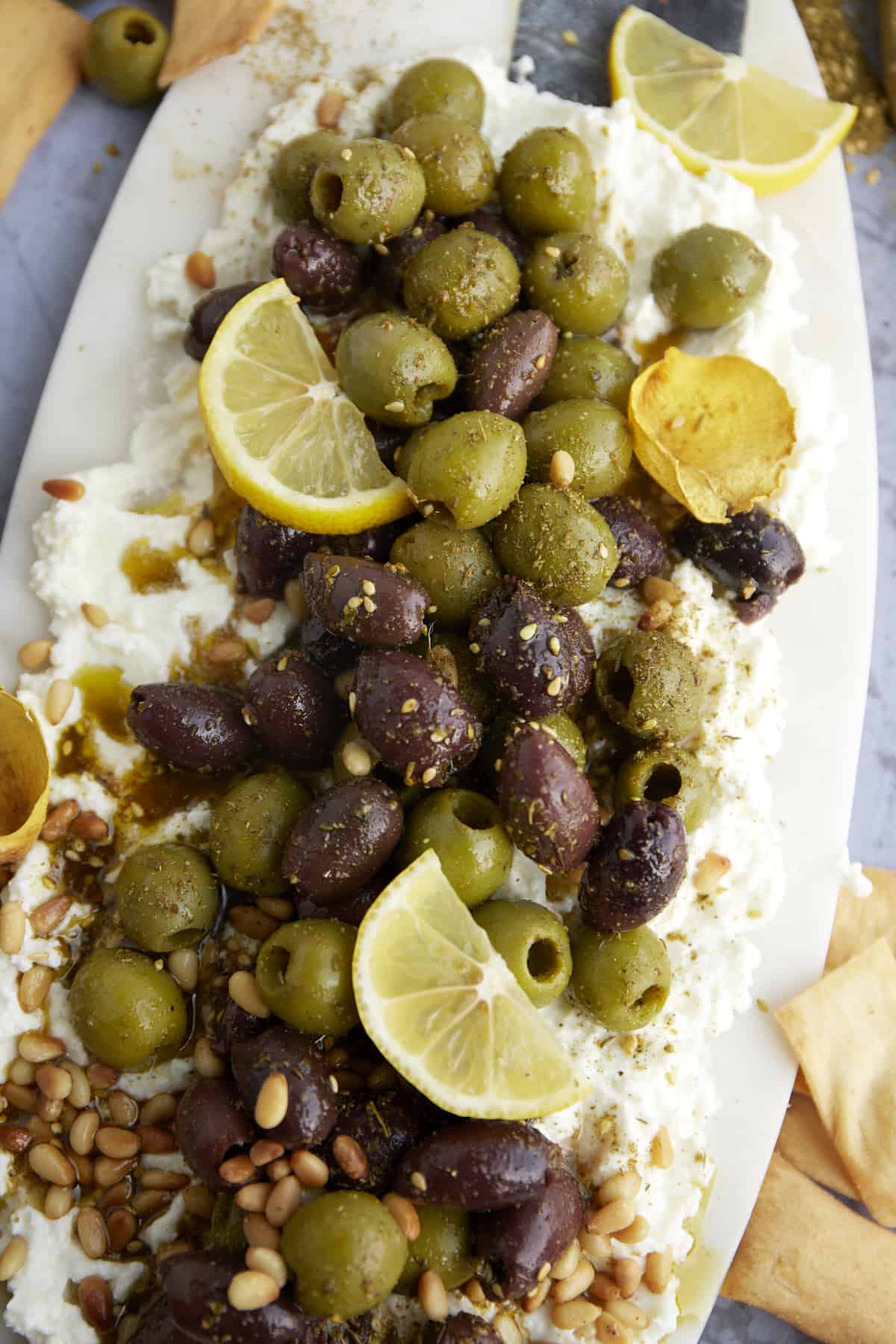 a feta board topped with marinated kalamata and green olives, lemon wedges, and seasonings