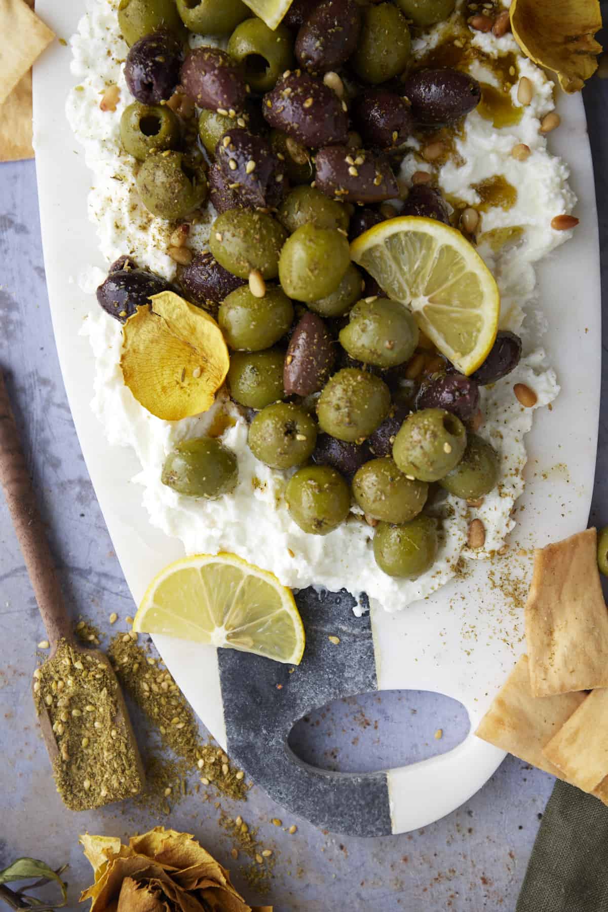 overhead image of a feta board topped with marinated olives, lemon wedges, and seasonings.