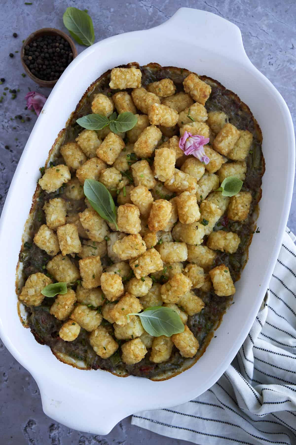 tater tot hotdish in a white casserole dish topped with fresh herbs