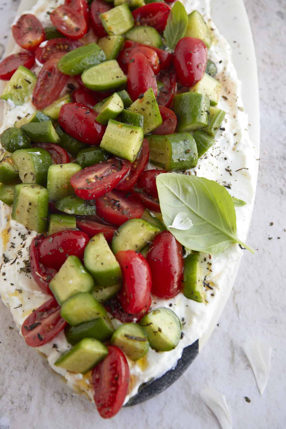 cucumber and tomato salad layered over whipped feta on a white serving platter